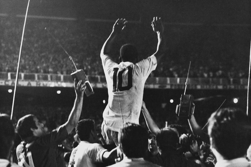 Pelé raises his arms as seen from behind raised above a crowd of people