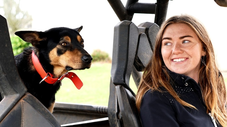 Claire sits at the wheel of the farm buggy smiling and looking at her kelpie Katie who sits in the back.