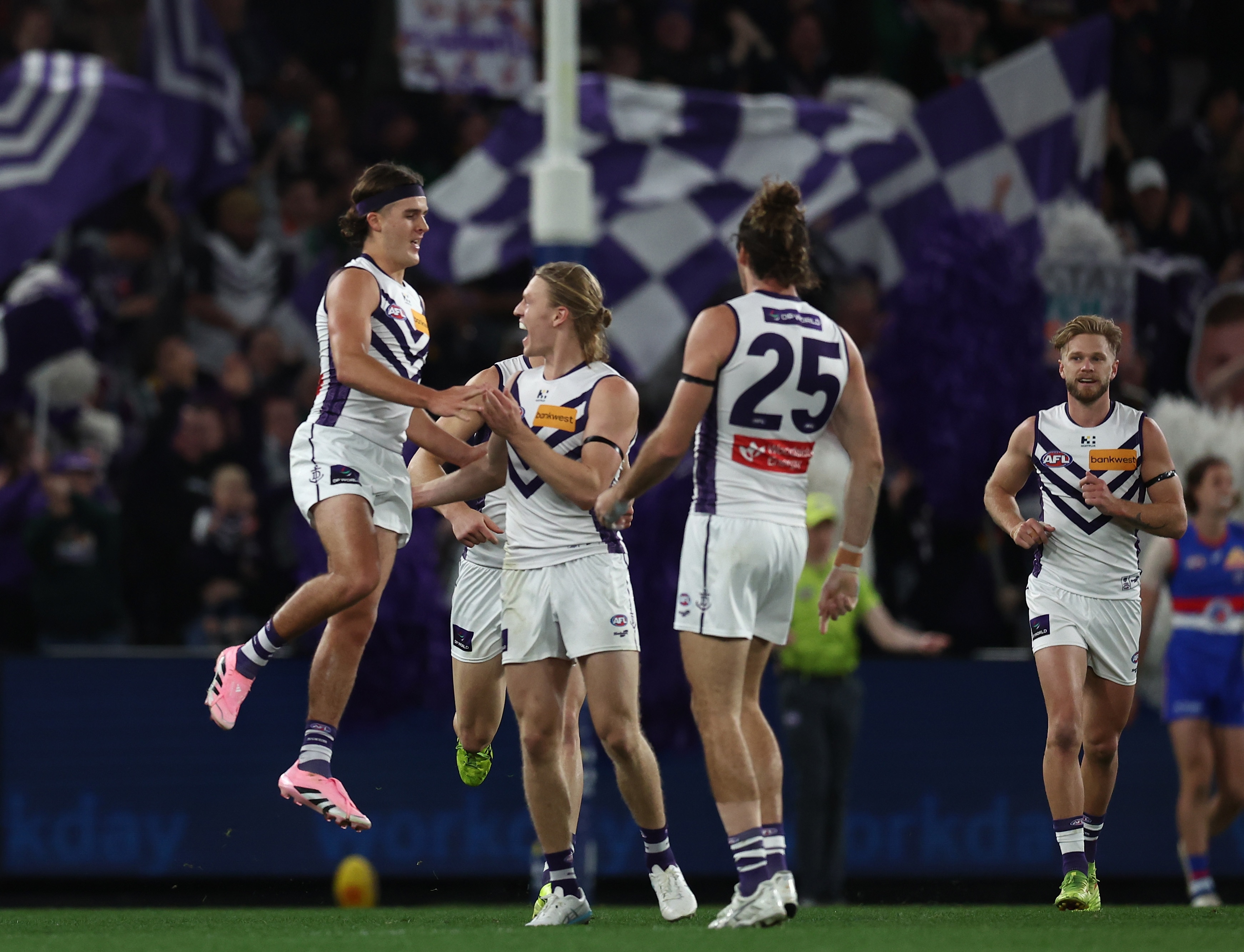 A group of AFL players in white celebrate a goal