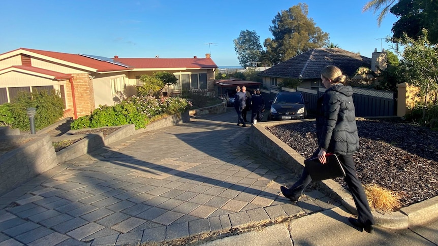 Police officers walking down a paved driveway outside a house