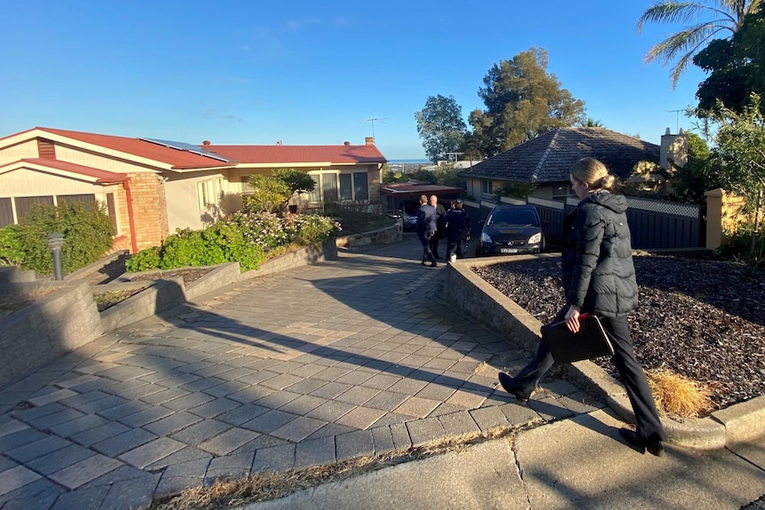 Police officers walking down a paved driveway outside a house