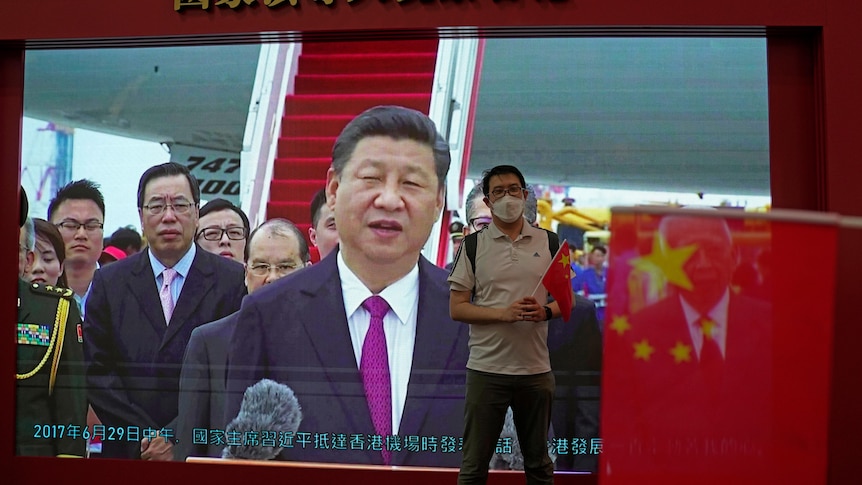 A visitor poses for a photograph in front of a TV showing Chinese president Xi Jinping