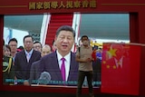 A visitor poses for a photograph in front of a TV showing Chinese president Xi Jinping