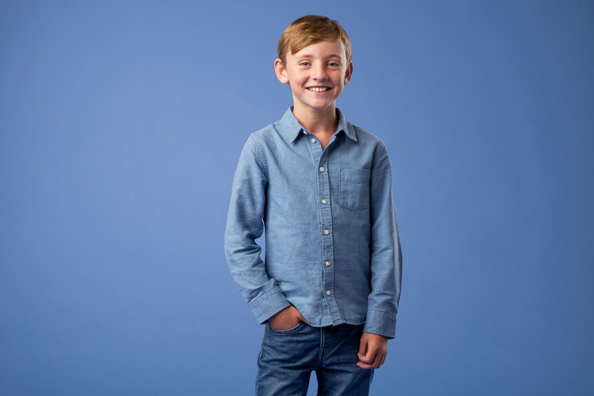 The face of this year's Jeans for Genes campaign, Archer Brady happily poses in jeans, a blue shirt against a blue background. 