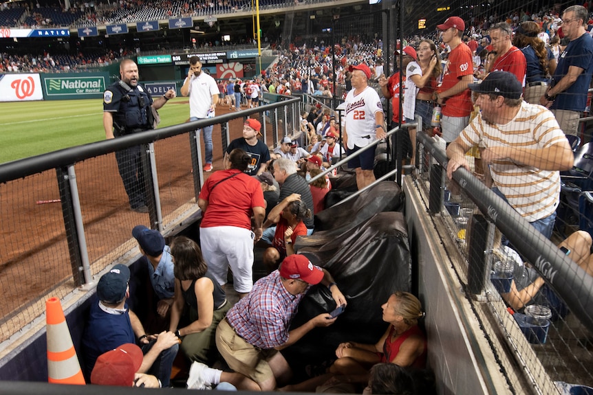 Fans take cover, crouching in the dugout as a policeman stands beside them on the field.