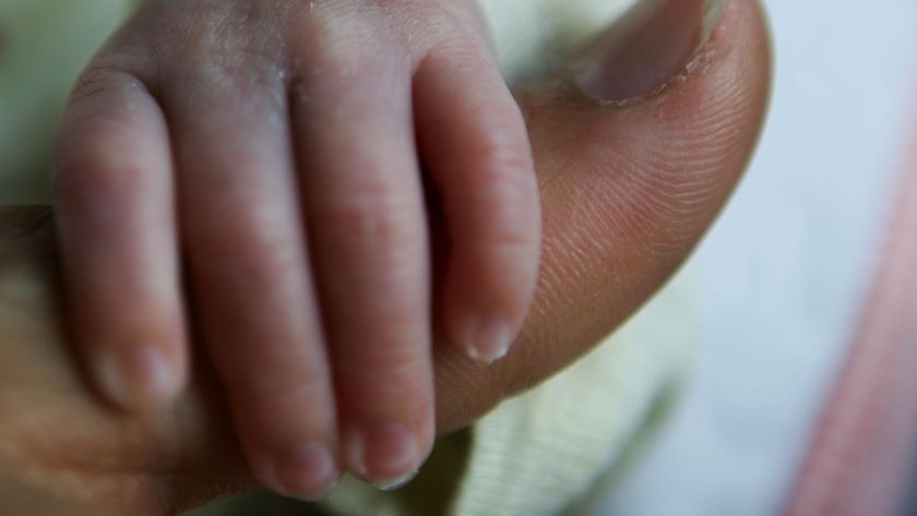 Baby holds mother's finger.