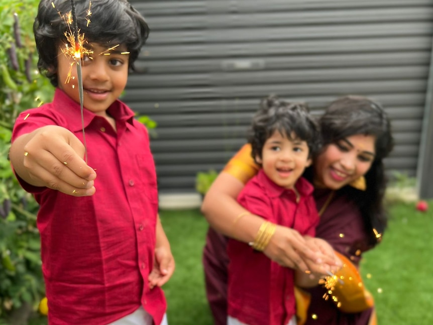 Preethi's son holds up a sparkler, while her other son watches on, excited.
