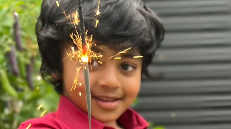 Boy in vibrant shirt holds up a sparkler, smiling