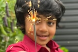 Boy in vibrant shirt holds up a sparkler, smiling