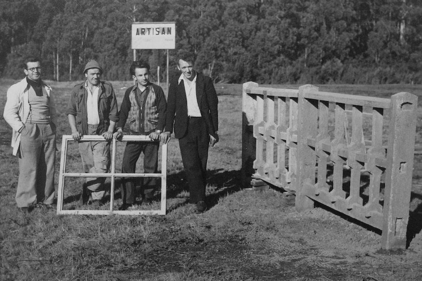 Old monochrome image of four men in 1950s, posing in front of a sign reading 'Artisan'.