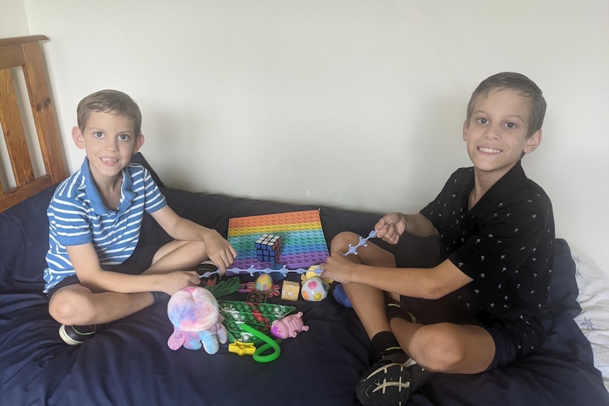 Declan and Jayden sitting on a bed with Declan's fidget toys laid out between them.