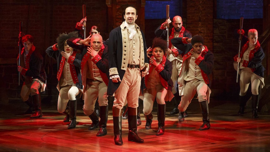 Cast from the original Broadway production of Hamilton, showing group of men and women in 18th-century costume on stage.