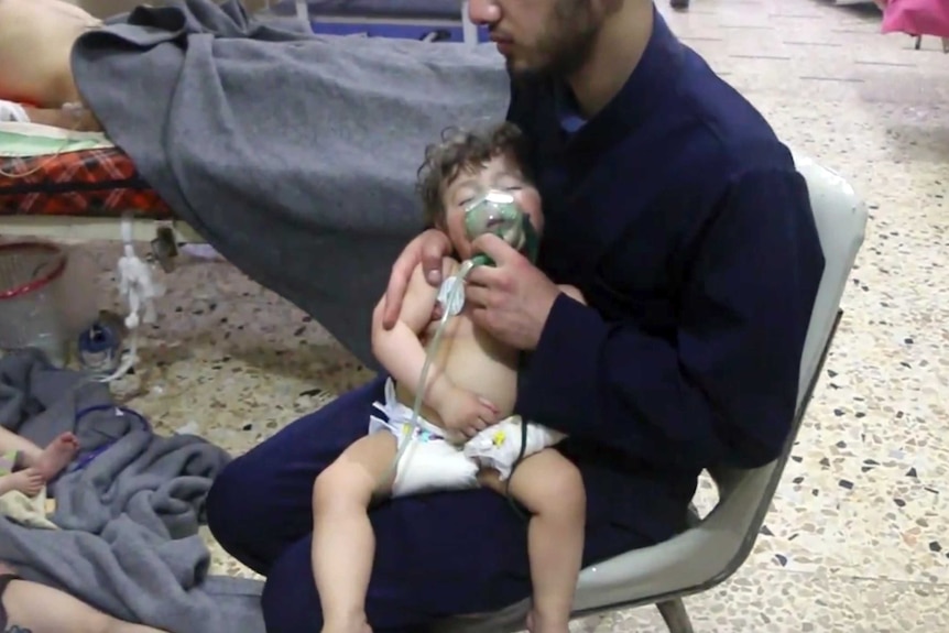 A medical worker gives a toddler oxygen. Someone is laying in a bed beside him. There are patients on the floor, one is a child.