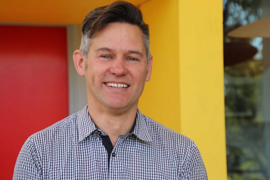 A head and shoulder shot of a smiling Brad Pettitt in front of a colourful red and yellow background.