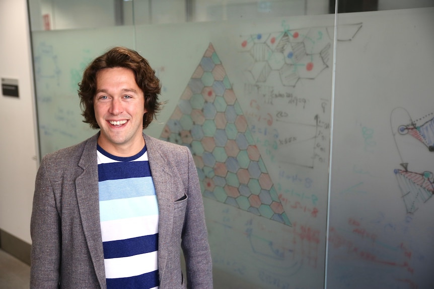 A man standing in front of a whiteboard with a triangular drawing and physics notations.