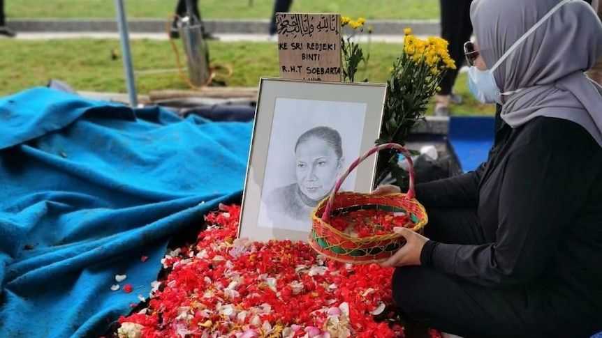 A woman scatters flower petals on a grave.