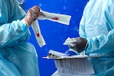 Two people in PPE swap medical testing kits.
