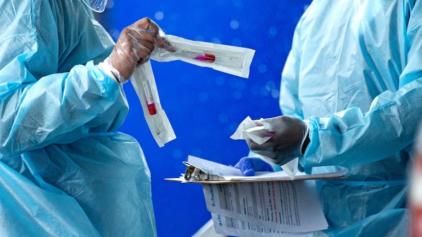 Two people in PPE swap medical testing kits.