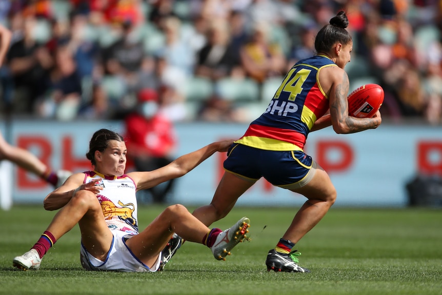 A Crows player holding the ball breaks free of a Lions player on the ground