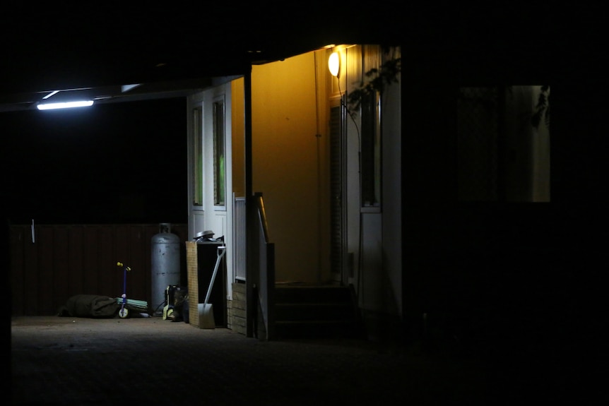 A house at night with the front light on and a child's plastic scooter at the front door.