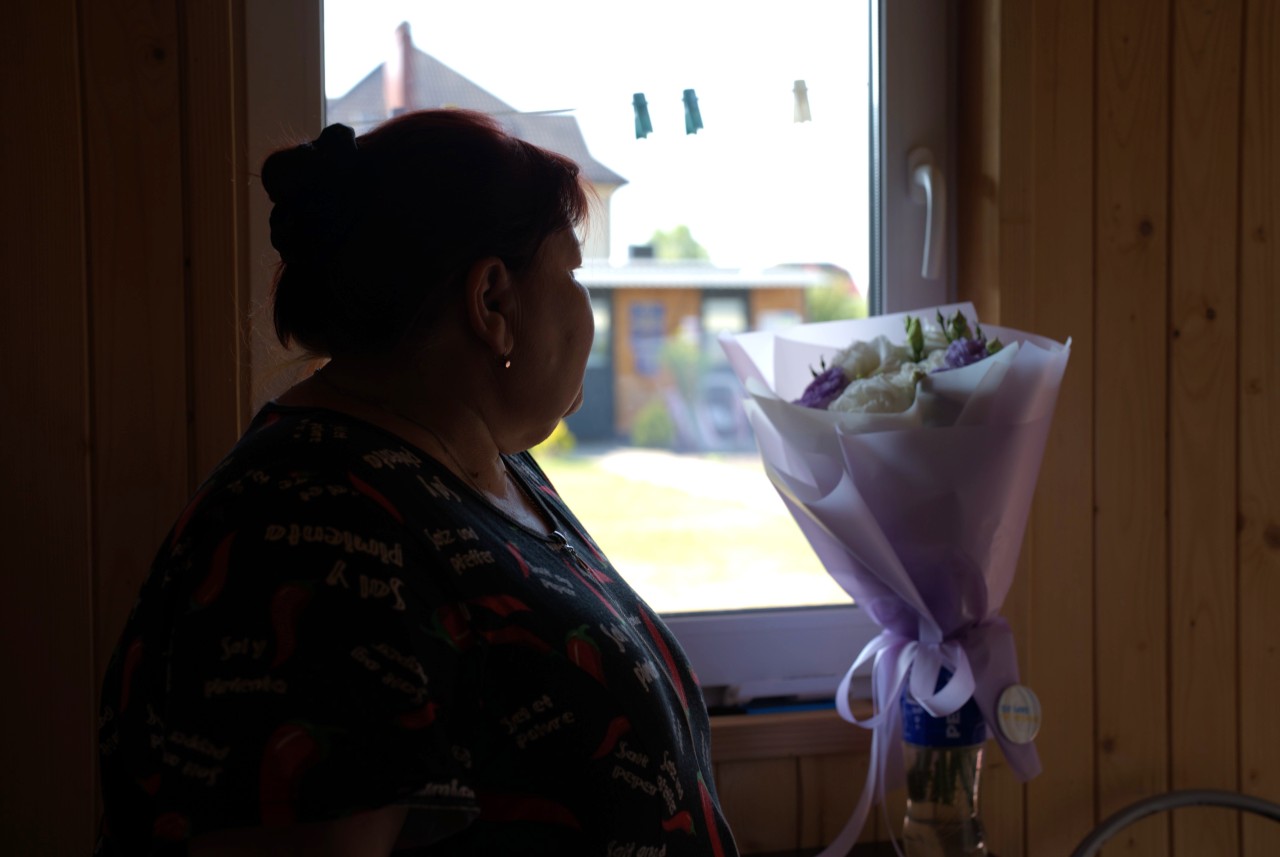 The silhouette of a woman with her head turned away from the camera, a bunch of flowers in front of her.