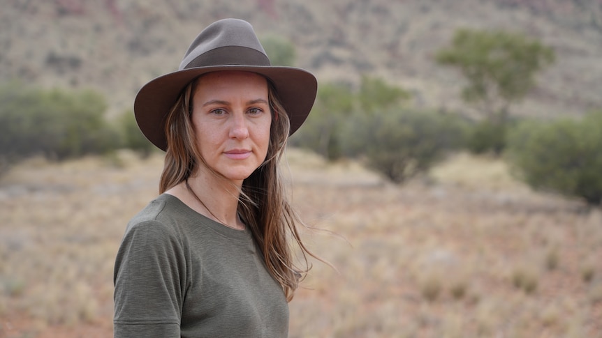 Woman in a green top and hat standing in a desert.
