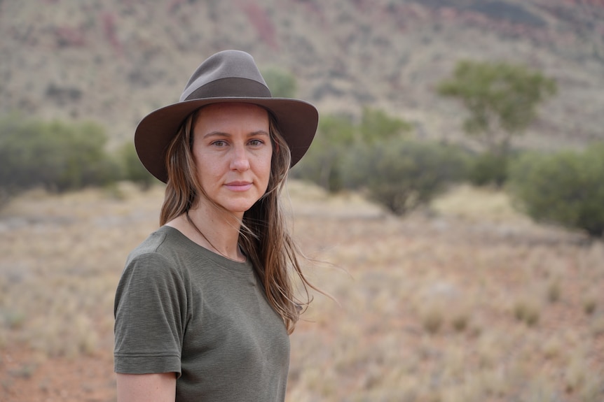 Woman in a green top and hat standing in a desert.