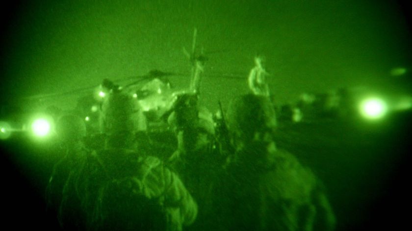 Night vision shot of US marines walking towards a Black Hawk helicopter during the launching of Oper