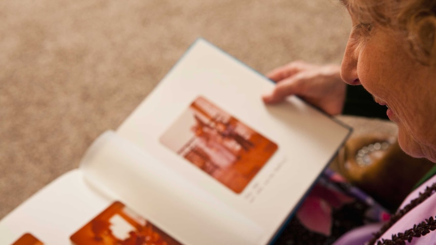 Over the shoulder of an older woman smiling at an out of focus photo album