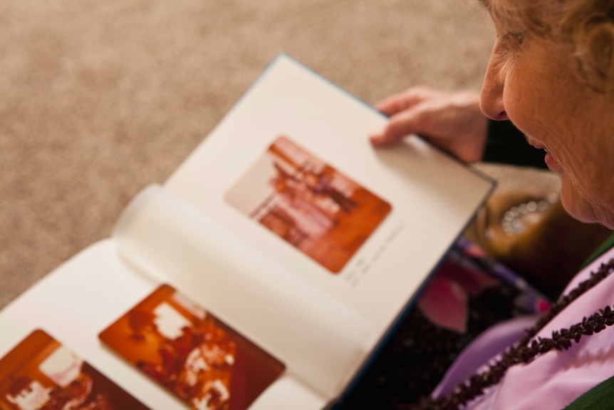 Over the shoulder of an older woman smiling at an out of focus photo album