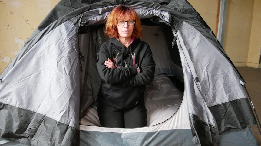 A woman with crossed arms and looking serious sitting in tent.