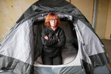 A woman with crossed arms and looking serious sitting in tent.