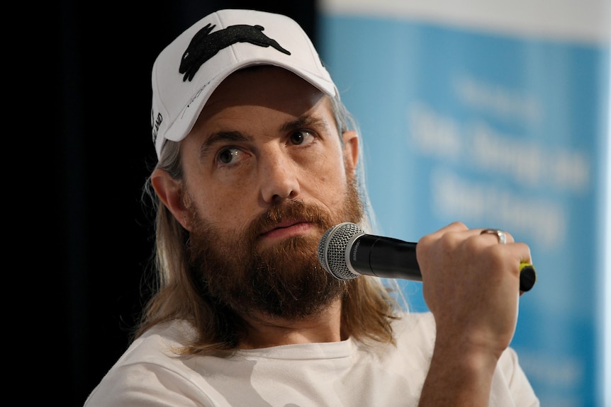 A man wearing a baseball cap and talking into a microphone