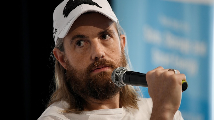 A man wearing a baseball cap and talking into a microphone