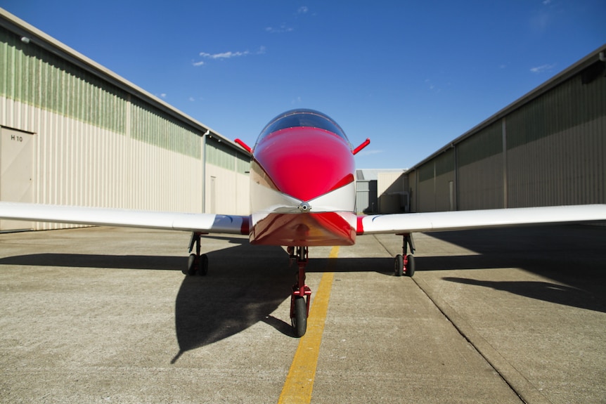 A small red-and-white jet between two hangars at Moruya Airport.