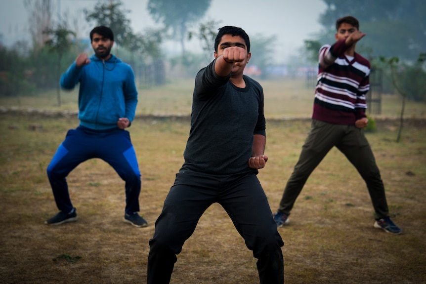 Three men in formation together do matching poses, one fist extended out in front