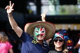 A man an woman, both wearing hats, the man wearing a red, gree, white wrestling mask, smiling.