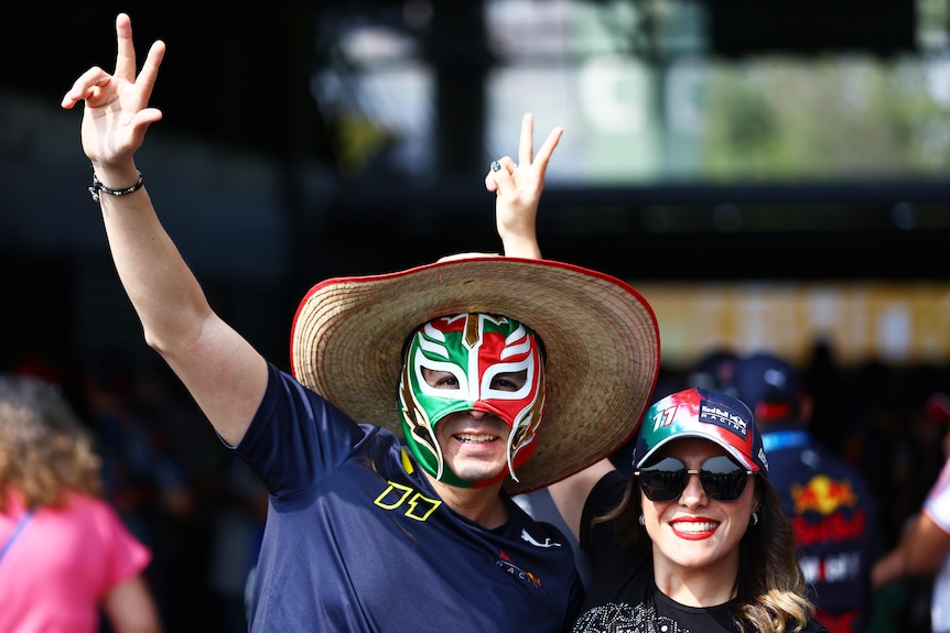 A man an woman, both wearing hats, the man wearing a red, gree, white wrestling mask, smiling.