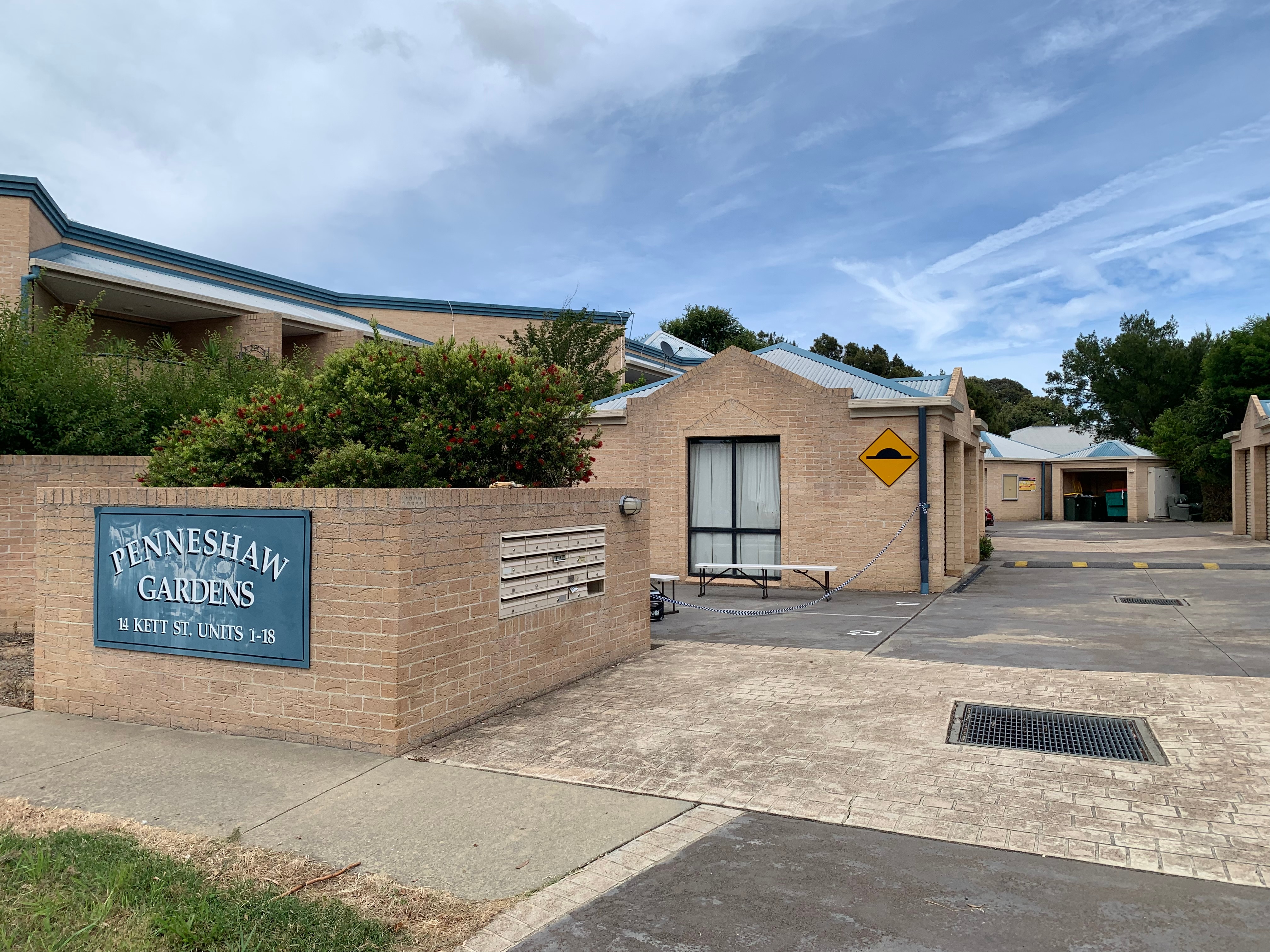 The outside of a housing complex, with a sign saying Penneshaw Gardens.