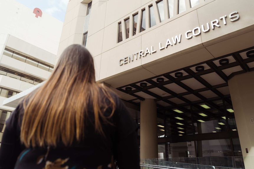 A woman in a black dress with flowers gazes up at the front of a court building.