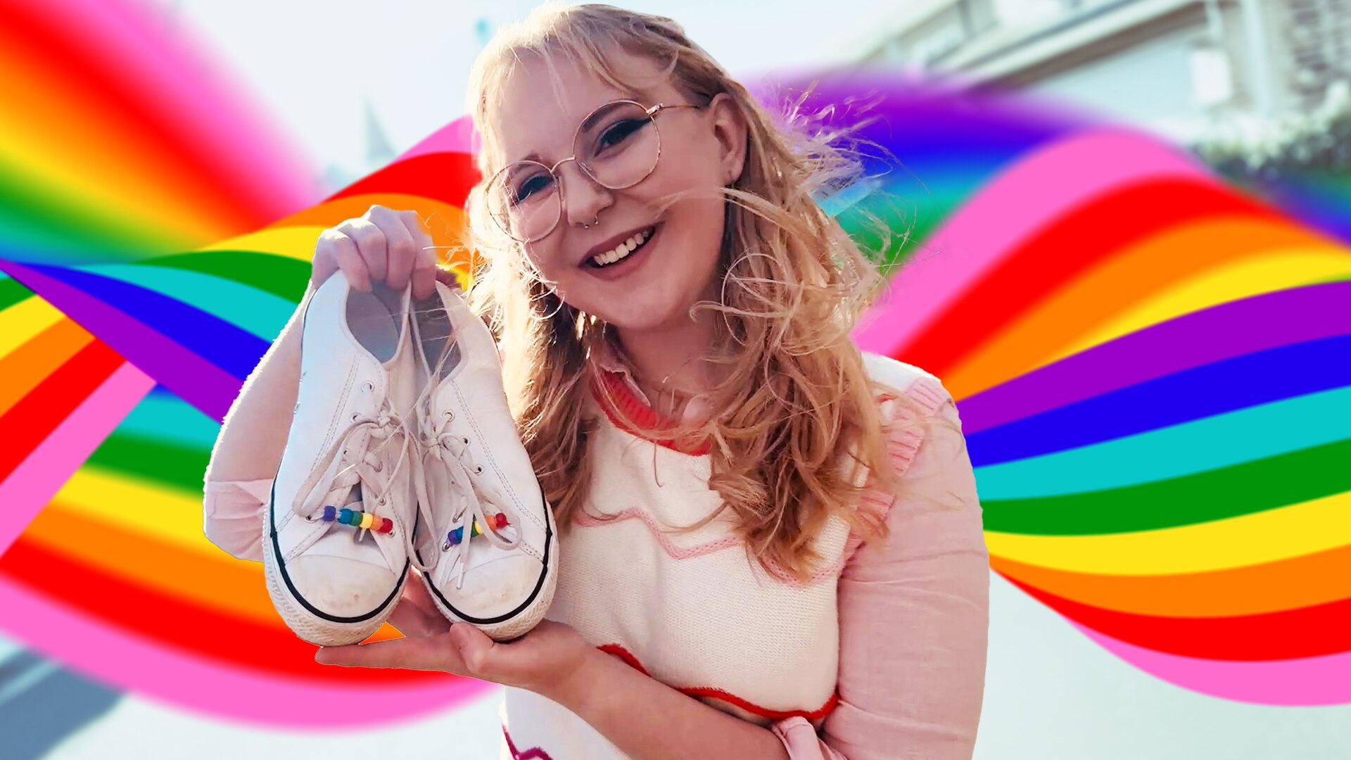 Abbie smiles and holds a pair of shoes up with rainbow beads in the shoelaces. Rainbow swirls in the background.