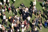 Crowd of people, with police in the middle, stand on grass