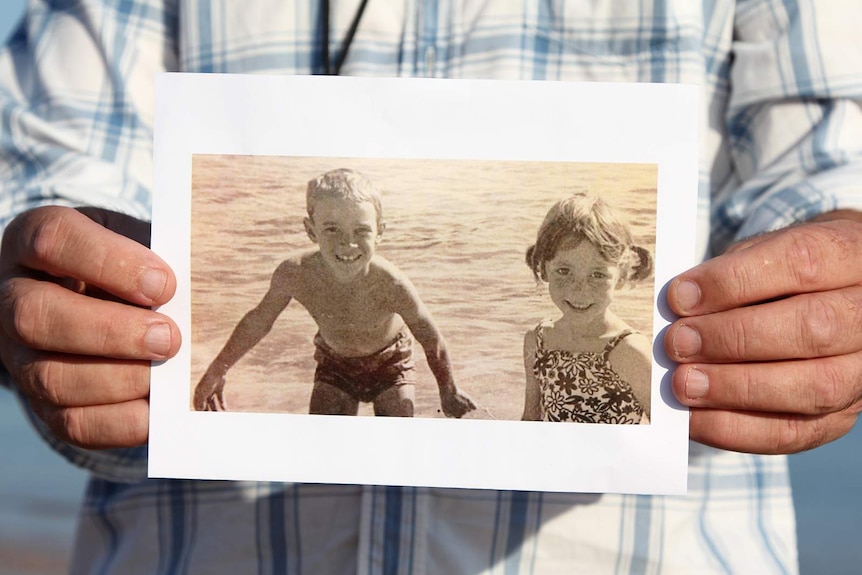 A photo of Michael Wells holding a vintage photo out to the camera.