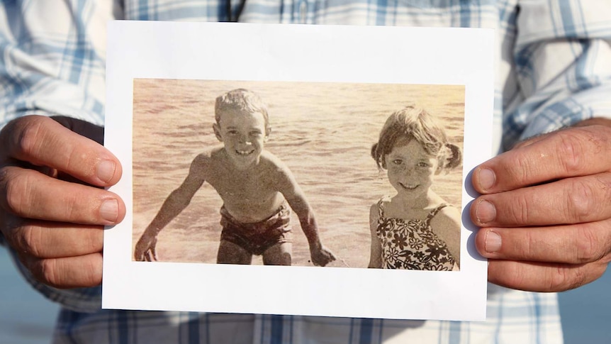 A photo of Michael Wells holding a vintage photo out to the camera.