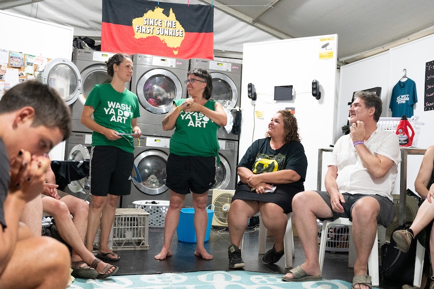 Two women speak to a group in a laundry.