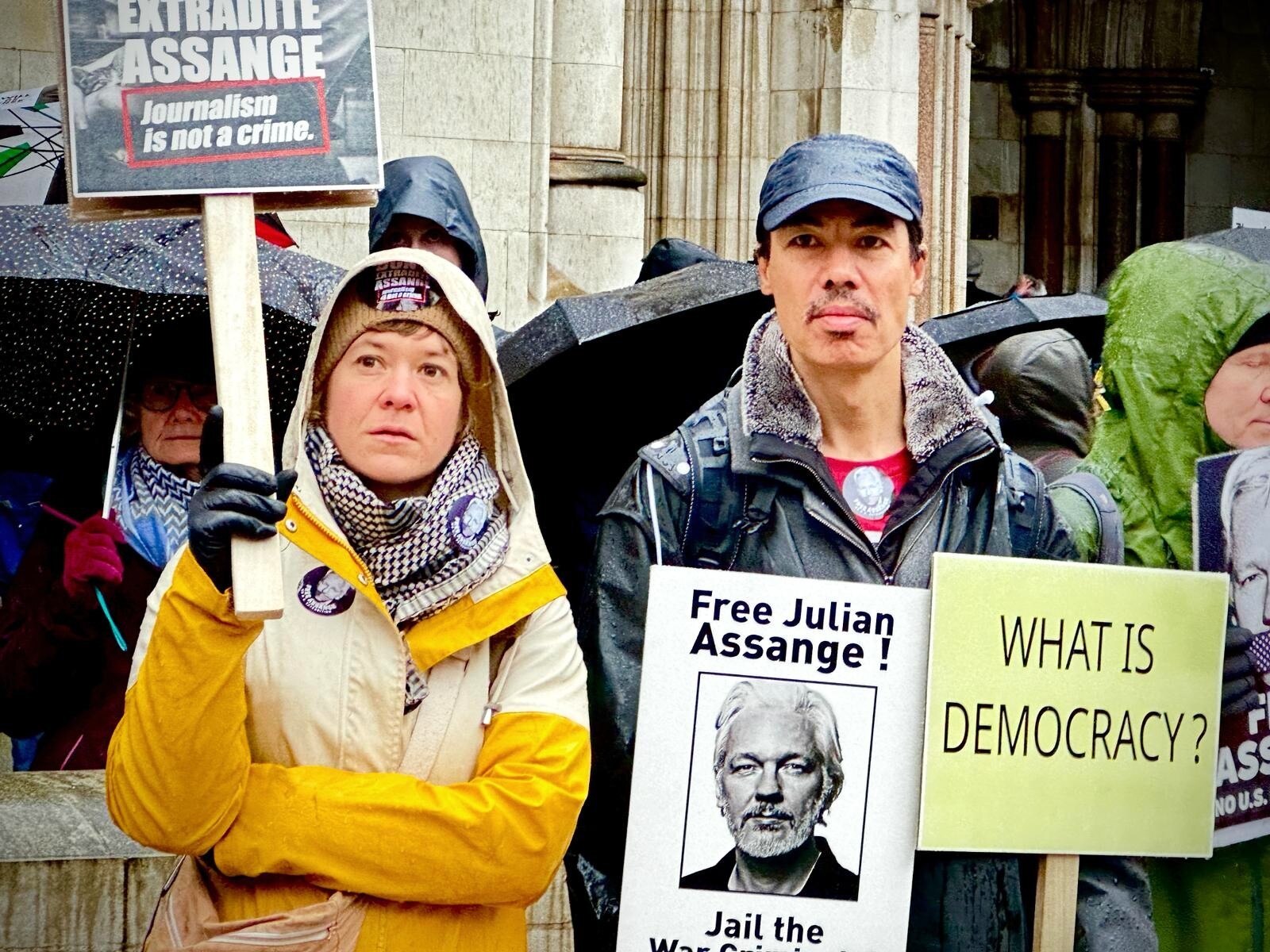 Two people with neutral expressions, holding signs, outside an old building