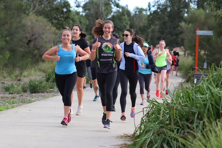 Two women run along a path and give two thumbs up.