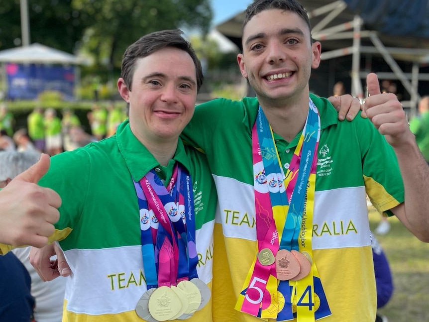 Two gymnasts wearing Team Australia tops smile at the camera wearing their medals from the Special Olympics.