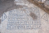 A mosac in white and blue tiles showing a Greek inscription.