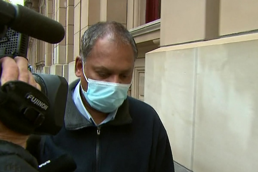 A man in a surgical mask walks along the footpath outside the Supreme Court building.